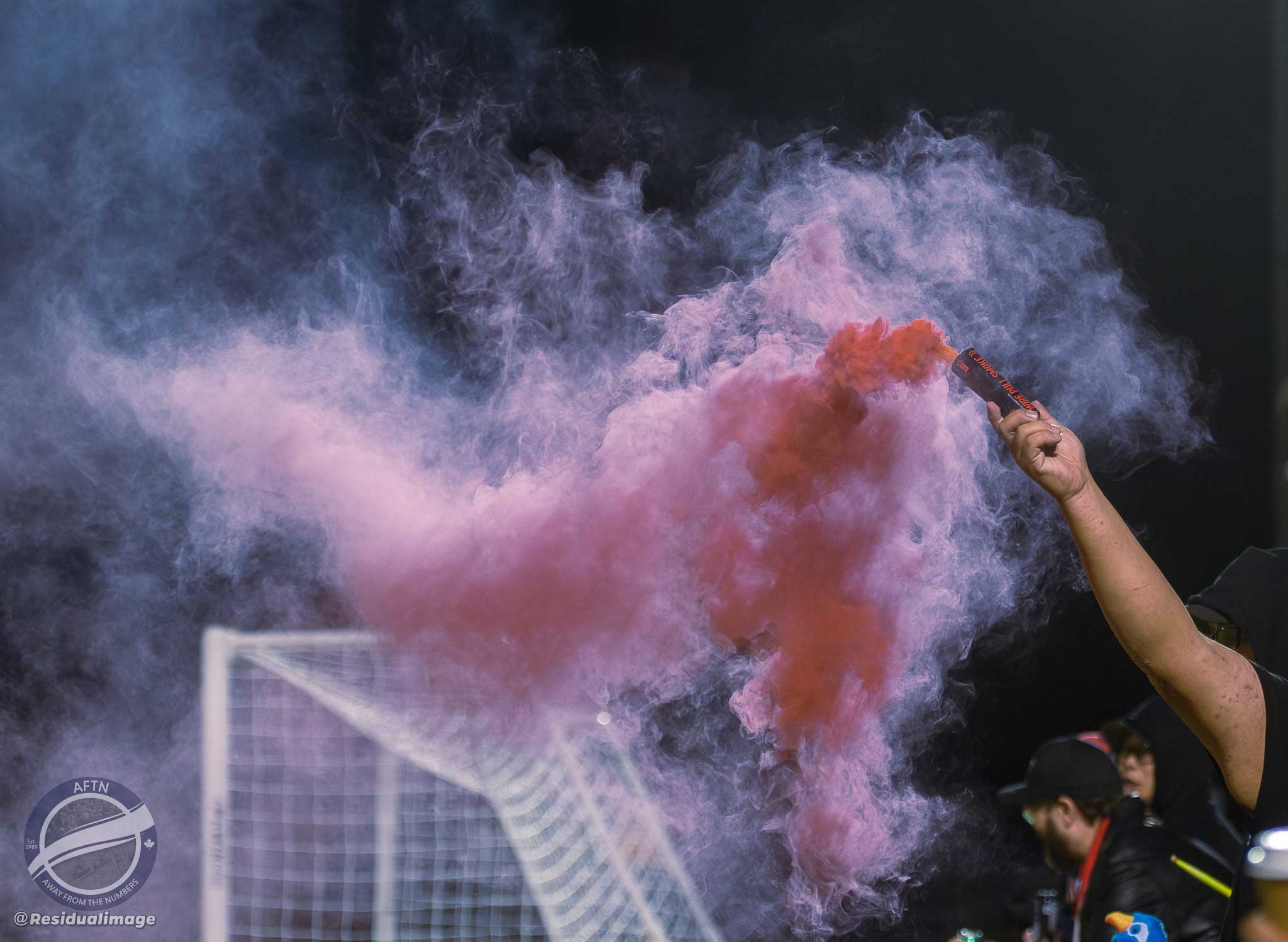 A hand holding a smoke grenade shooting red smoke in the air